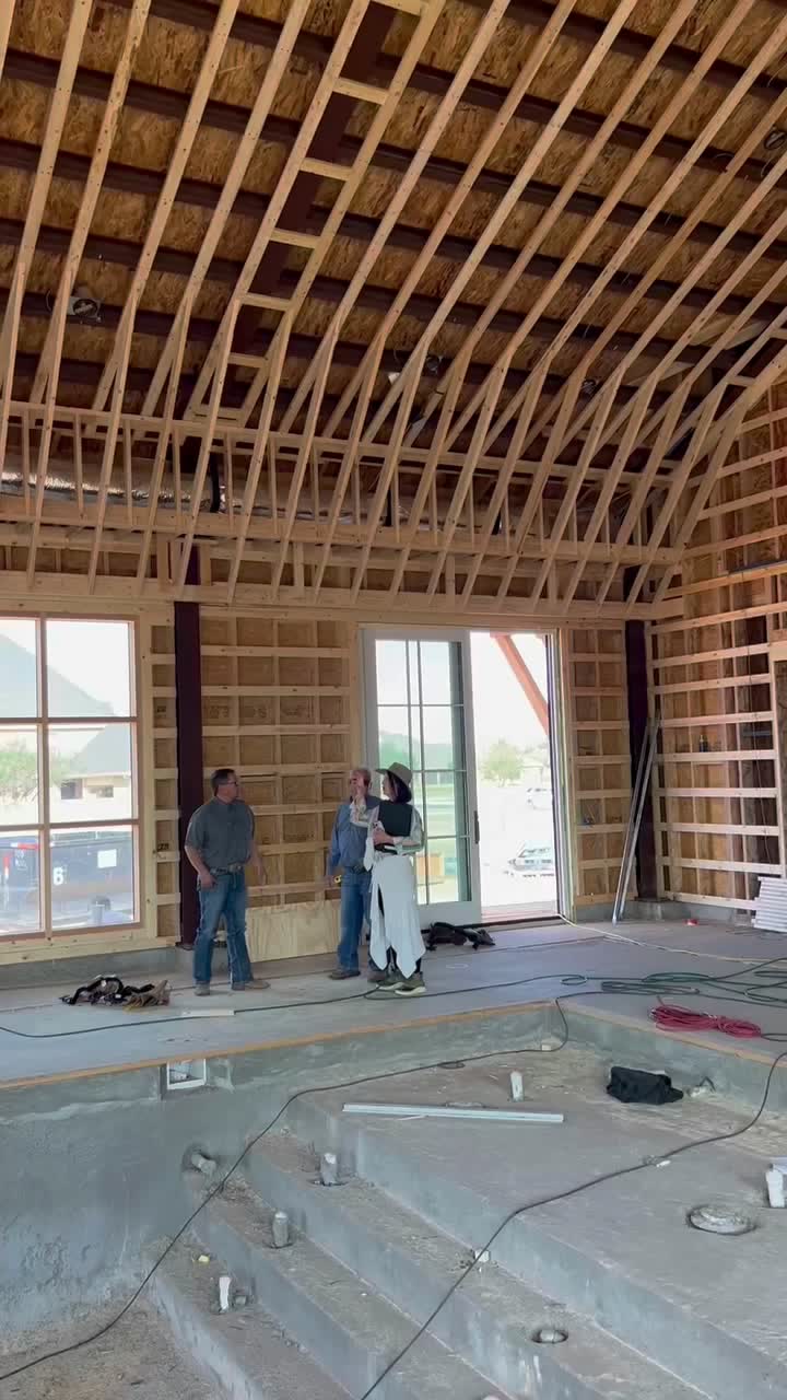 Open framing under a vaulted roof at rough-in, with plumbing stubbed up through the floor.