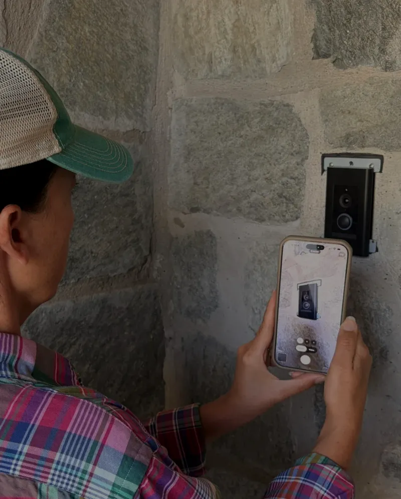 On site, Kristina photographs a doorbell back plate on a stone wall with Co|See Studio, to add it to the project's punch list.