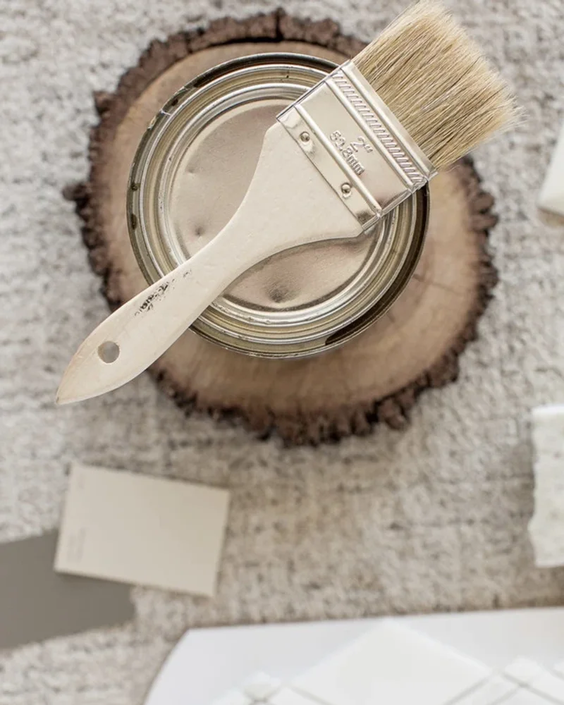 A paint can with a brush across it on a wood slice, beside paint chips and a marble tile sample.